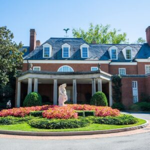 Stately home with columns and a small garden and statue in the center of a circular drive.