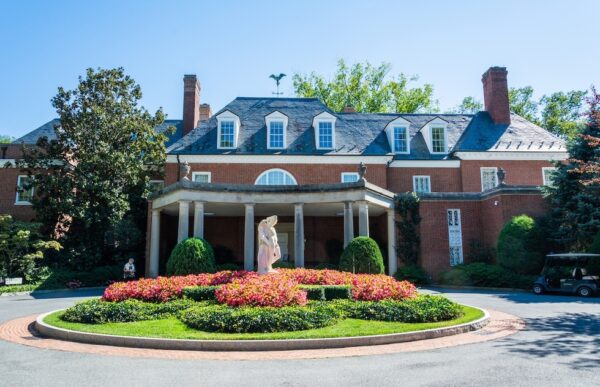 Stately home with columns and a small garden and statue in the center of a circular drive.